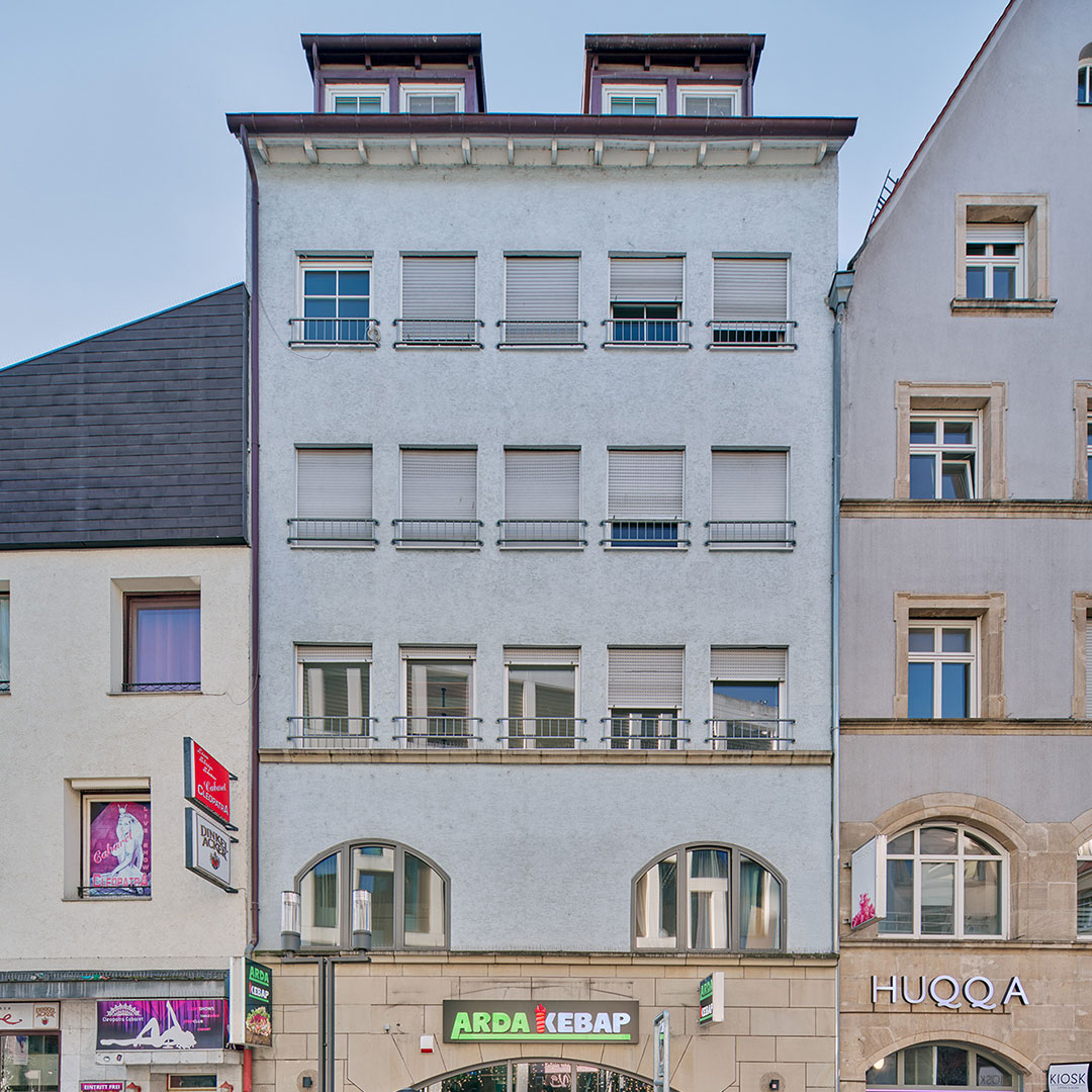 A four-story building with closed gray shutters, two dormer windows on the roof, and a green ARDA KEBAP sign at street level, flanked by neighboring buildings and shops.